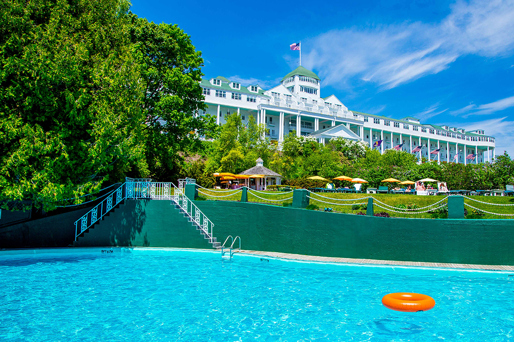 Image of the Esther Williams Swimming Pool with glistening bright blue pool and views of the property. Grand Hotel, a member of Historic Hotels since 2001, dates to 1886. It is located in Mackinac Island, Michigan.